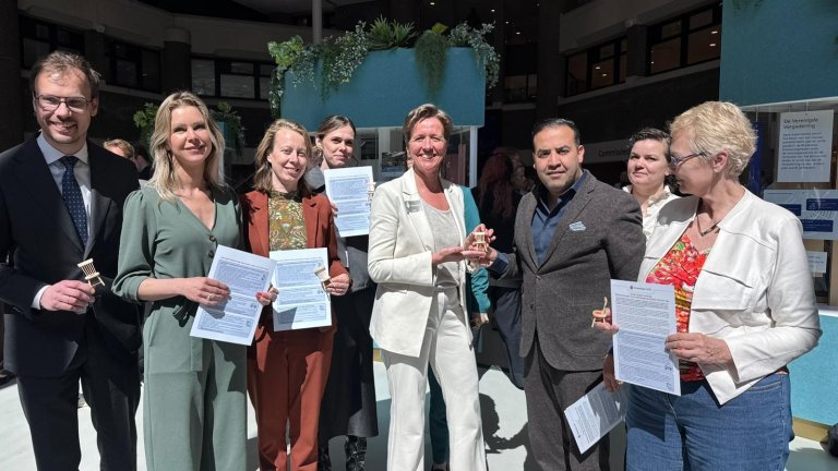 Chair Mohammed Mohandis receives a miniature chair from Tessa Roseboom. A selection of the members of the Standing Committee on Health, Welfare and Sport (VWS) are holding the manifesto.
